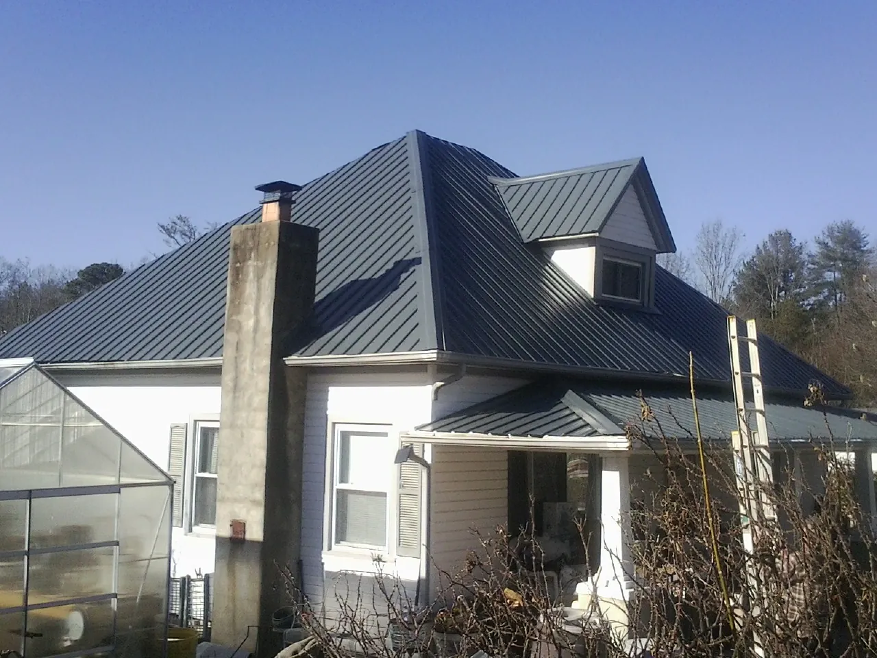 Dark blue standing seam metal roof on a white farmhouse with dormer — Slate & Tile Roof Repair by Roofing Brothers in Waupaca