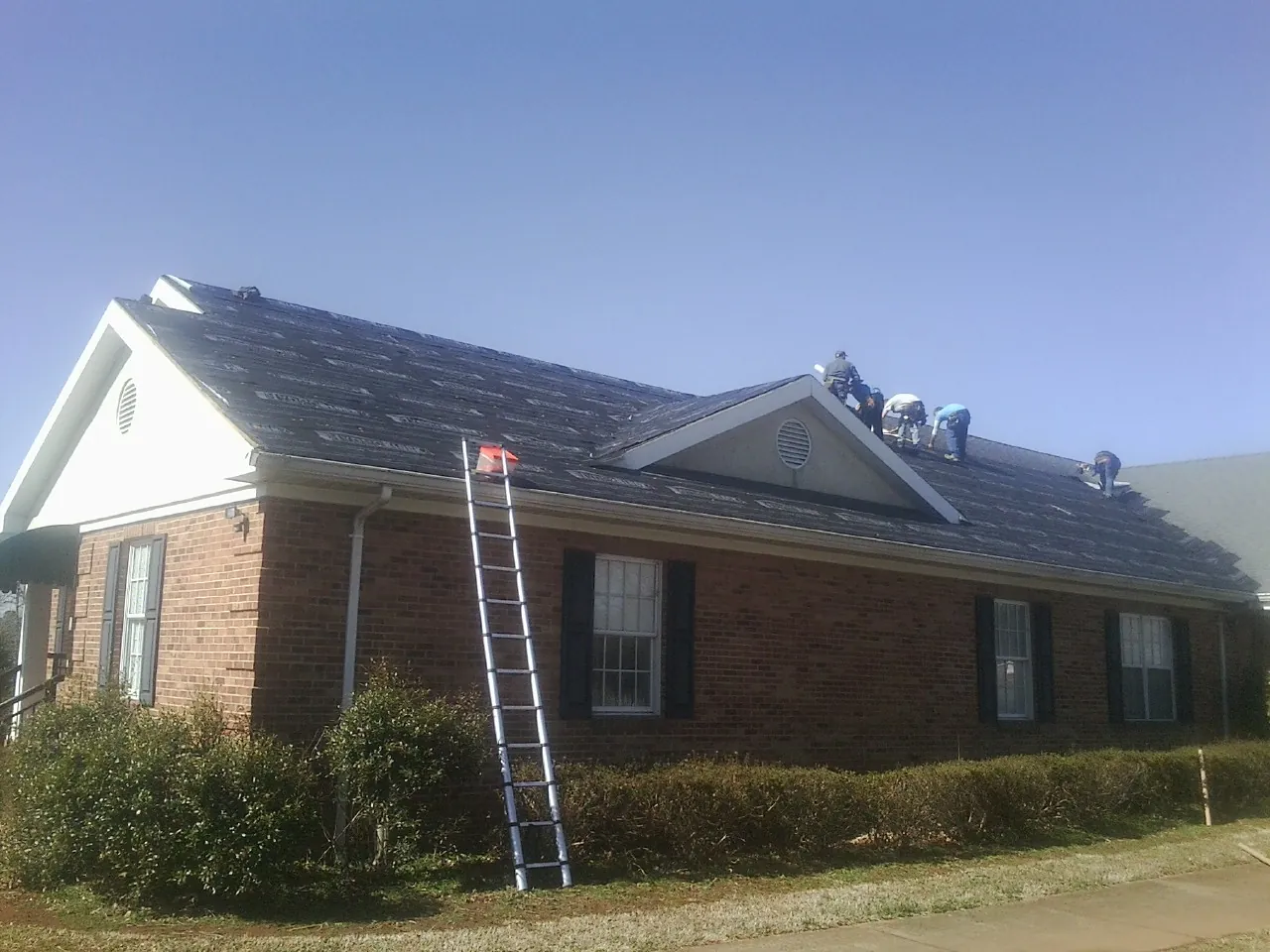 Crew tearing shingles off a brick ranch roof with a ladder set — Emergency Roof Repair work by our crew in Waupaca