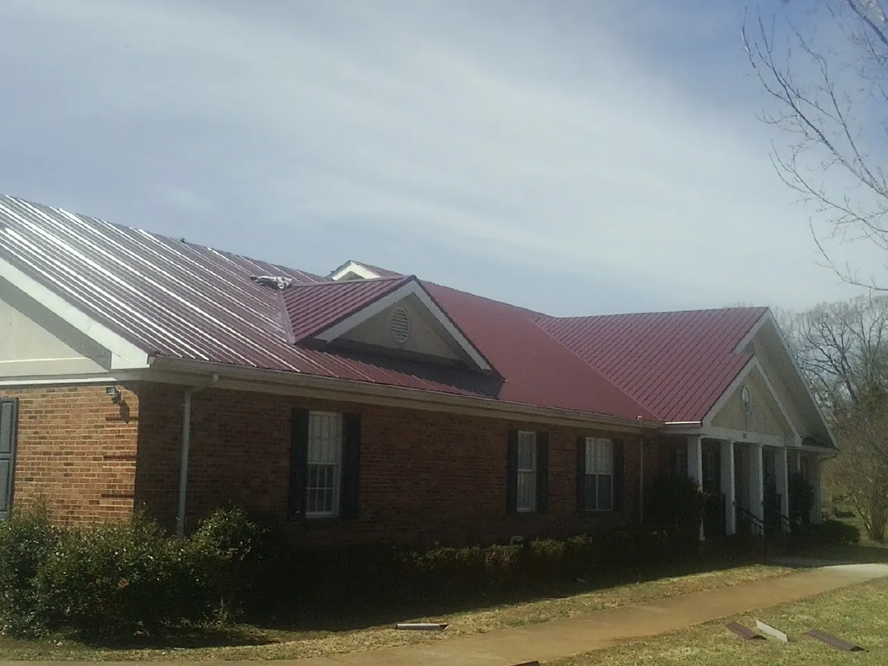 Red metal roof with gabled entries on a long brick building, from a Hail Damage Roof Repair job in Waupaca