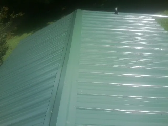 New green metal panels meeting at the ridge of a roof — Flat Roof Repair work by our crew in Waupaca