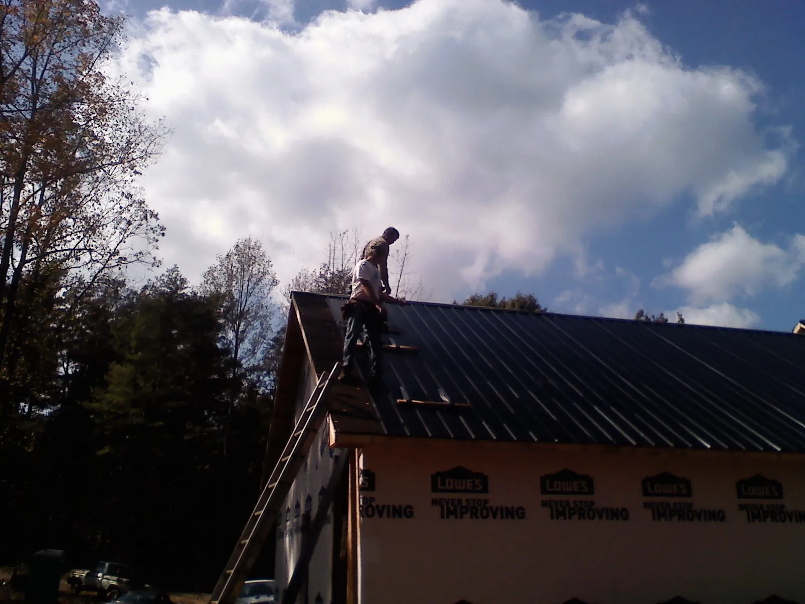 Roofer fastening dark metal panels high against a cloudy sky, from a Roof Inspection job in Waupaca