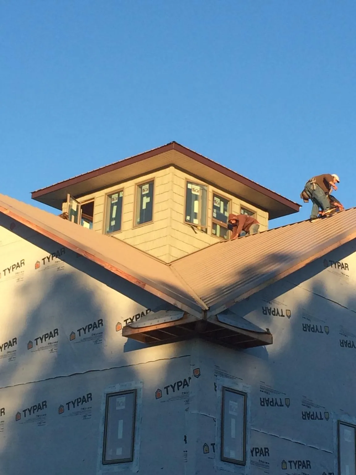 Roofers working around a rooftop cupola on a new metal roof at sunset — Roof Waterproofing in Waupaca by Roofing Brothers